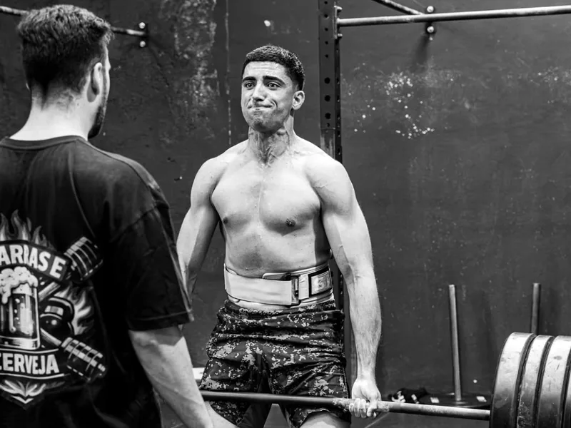 Atleta de Cross Box APH con cinturón, sujetando la barra cargada en el peso muerto, con el coach delante