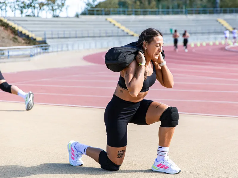 Atleta de Cross Box APH haciendo zancadas con saco de arena en una pista de atletismo
