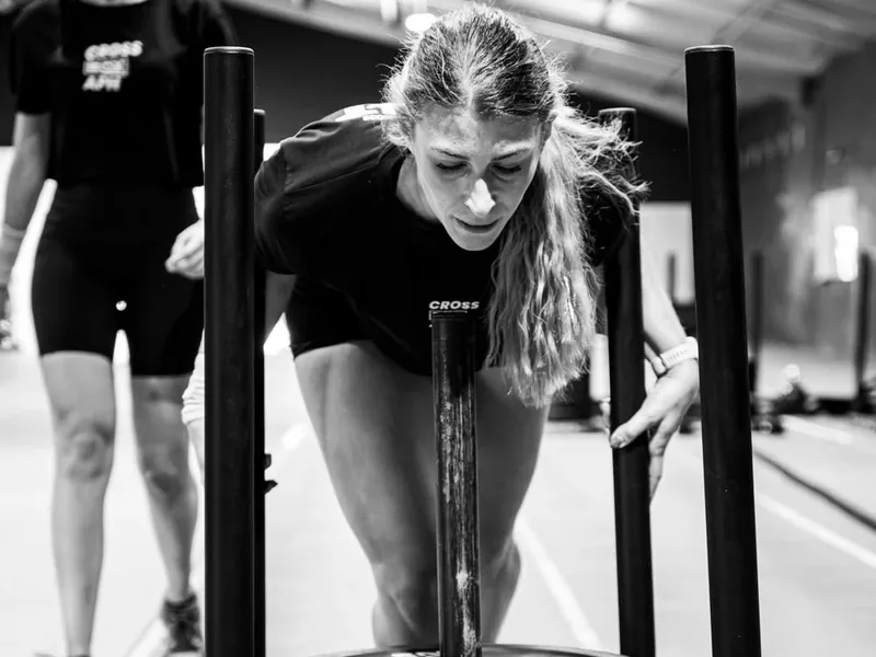 Atleta de Cross Box APH empujando el sled cargado, con una compañera detrás